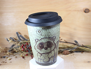 A green ceramic mug with a raccoon engraved on it looking cute